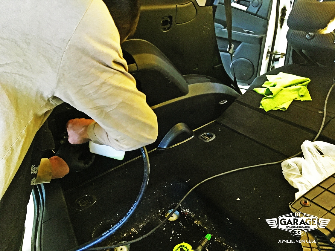 На фото мастер «DT GARAGE 33» чистит обивку салона автомобиля под сиденьями.