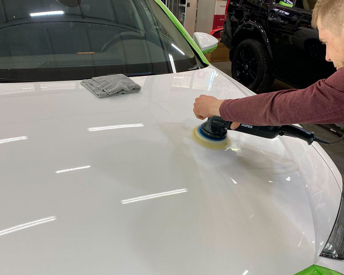 Смотреть на фото: процесс полировки капота белого цвета у машины Audi A6.
